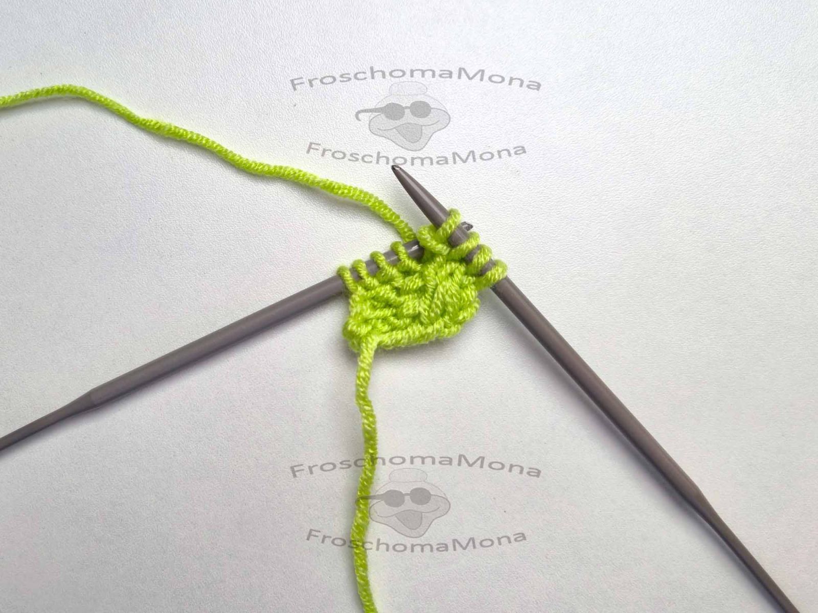 Das grüne Strickstück auf weißem Untergrund zeigt die Zunahme am Anfang der Reihe.