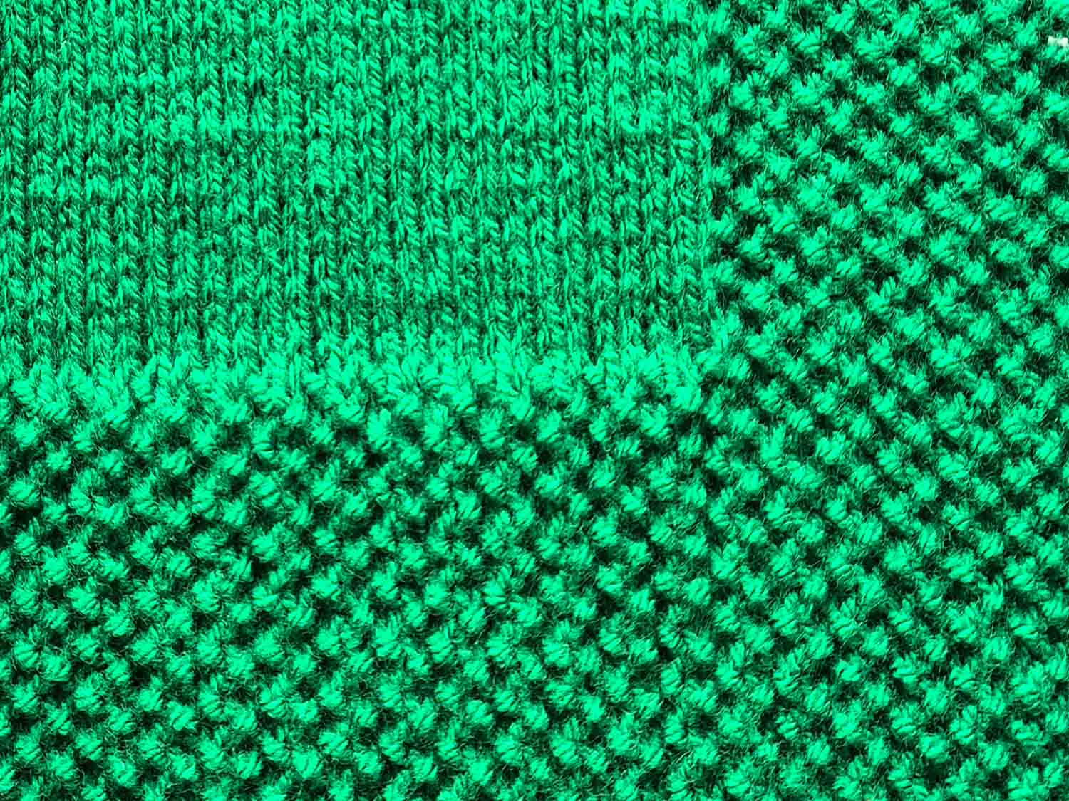 Ein gestrickter Deckenrand im Perlmuster aus grüner Wolle ist zu sehen.