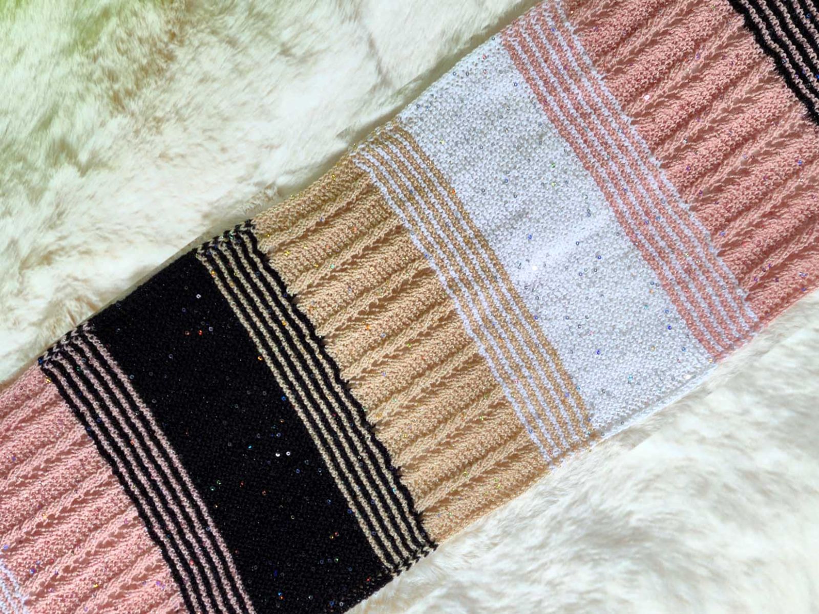 Ein Schal in 4 Farben und verschiedenen Mustern liegt schräg auf einem Fell.