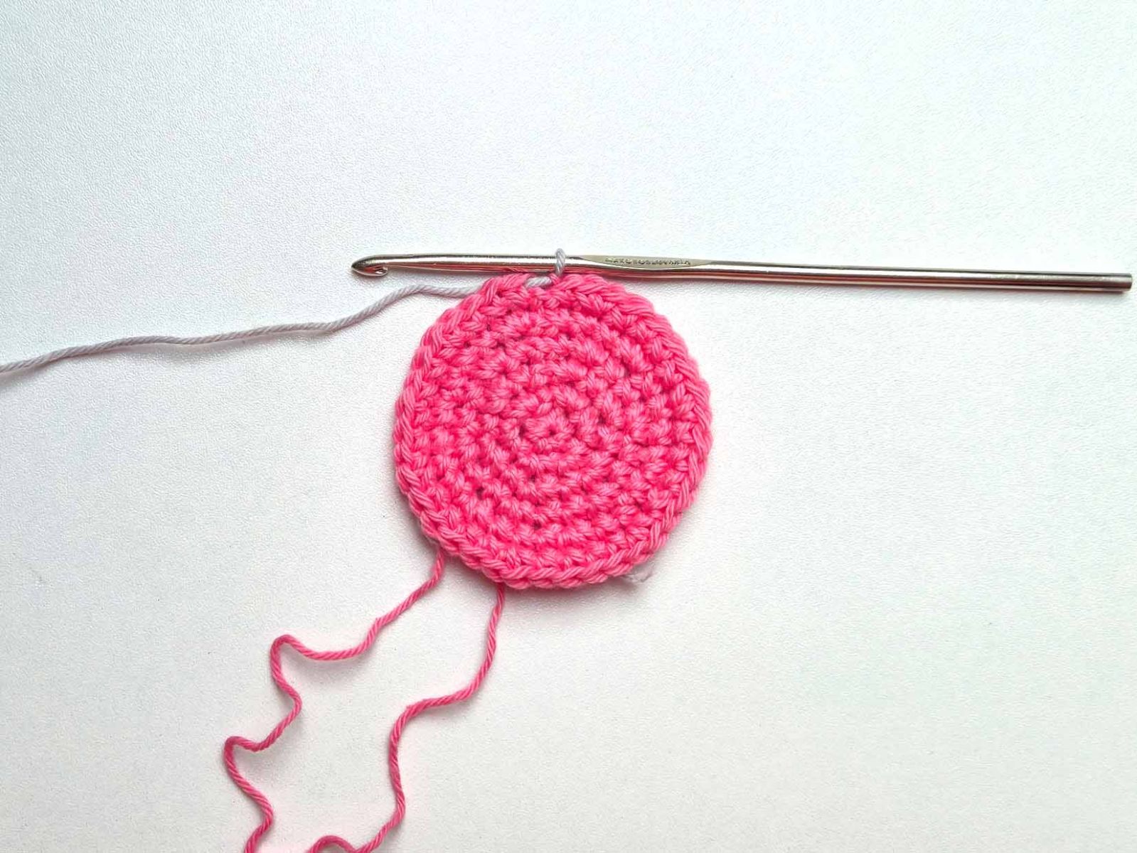 Das Bild zeigt das pinke Häkelstück nach Beenden der Runde 6. Die Kettmasche wurde mit bereits mit der 2. Farbe grau gehäkelt.