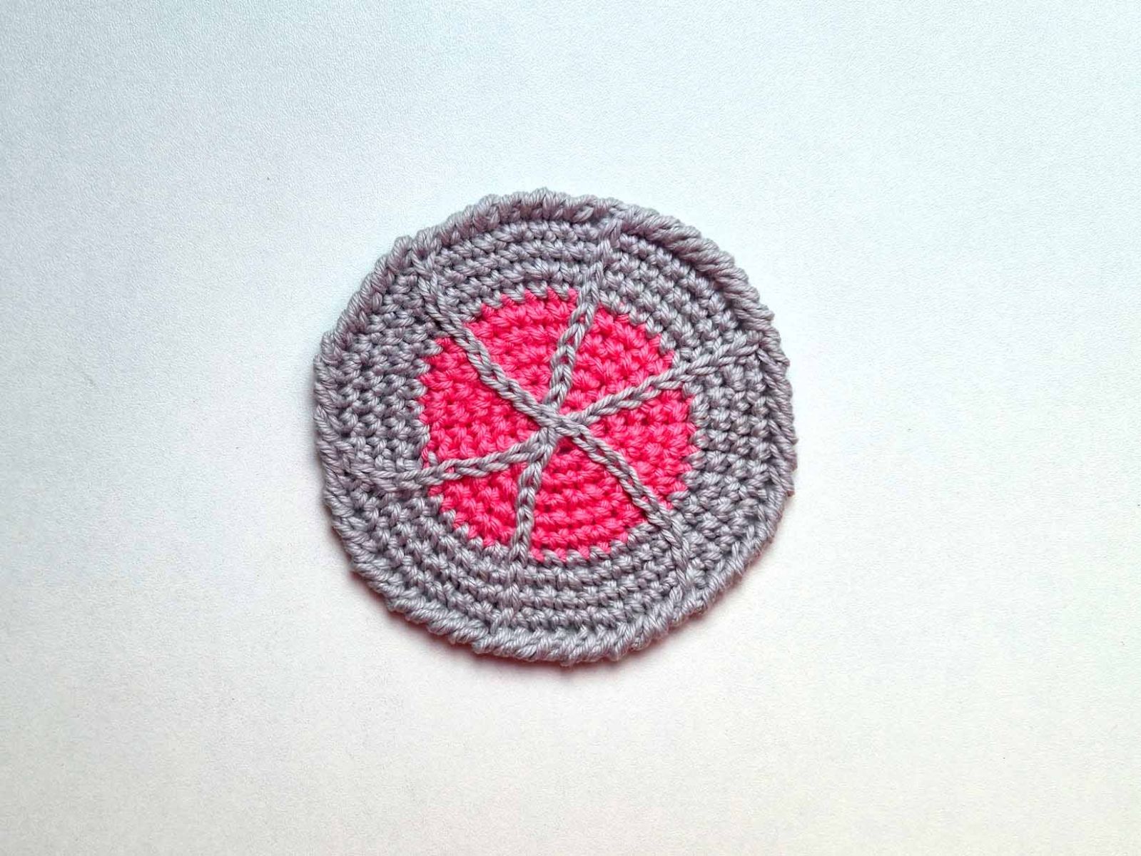 Das Bild zeigt den fertig gehäkelten Untersetzer in pink und grau.