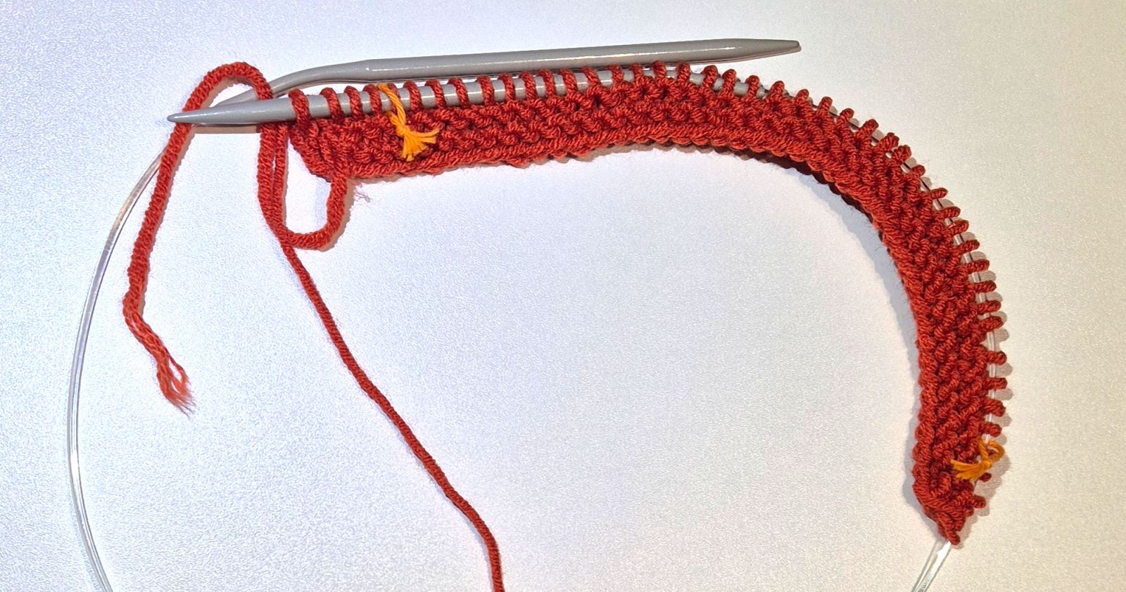 Der Anfang des Strickstücks mit Maschenmarkierern ist zu sehen.
