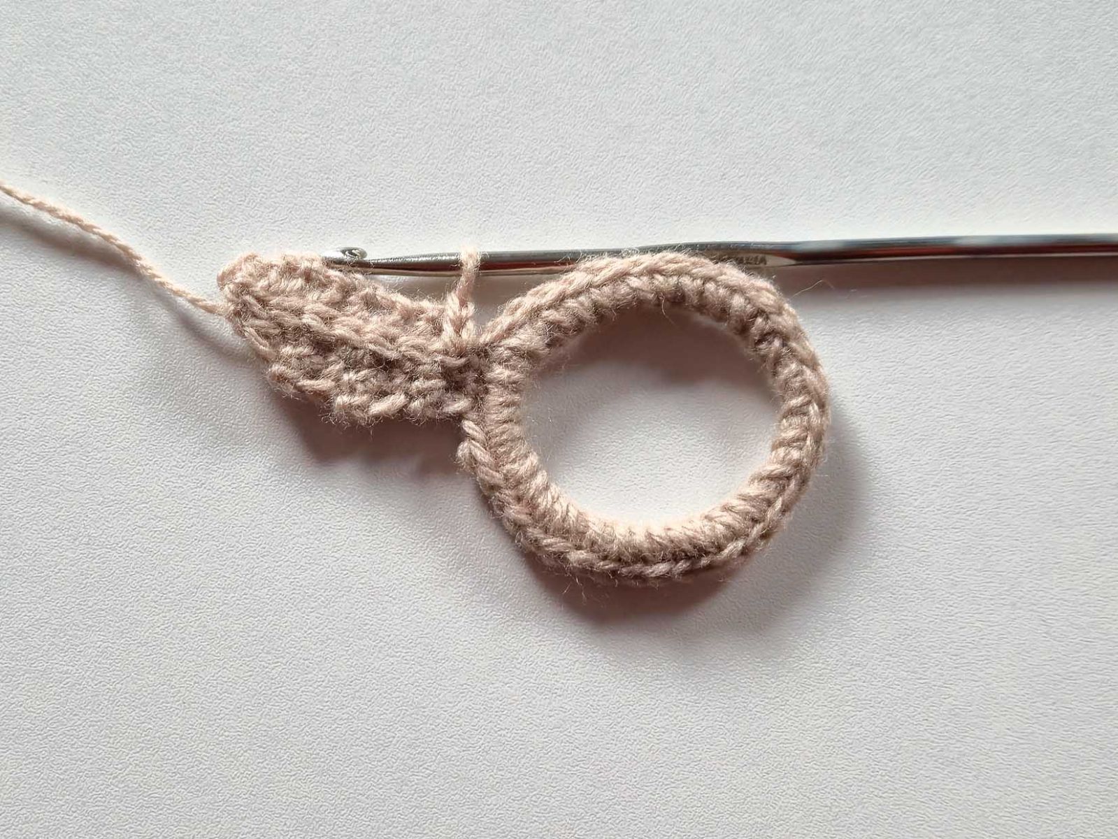 Das Bild zeigt nun mit beigem Faden wie die Maschenkette auf dem Ohr fertig aussieht.