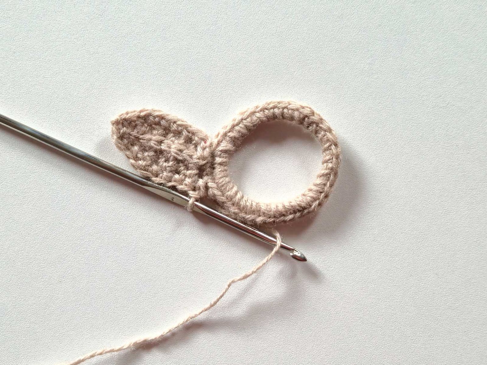 Das Bild zeigt, wie das beige Ohr mit festen Maschen umhäkelt wurde.