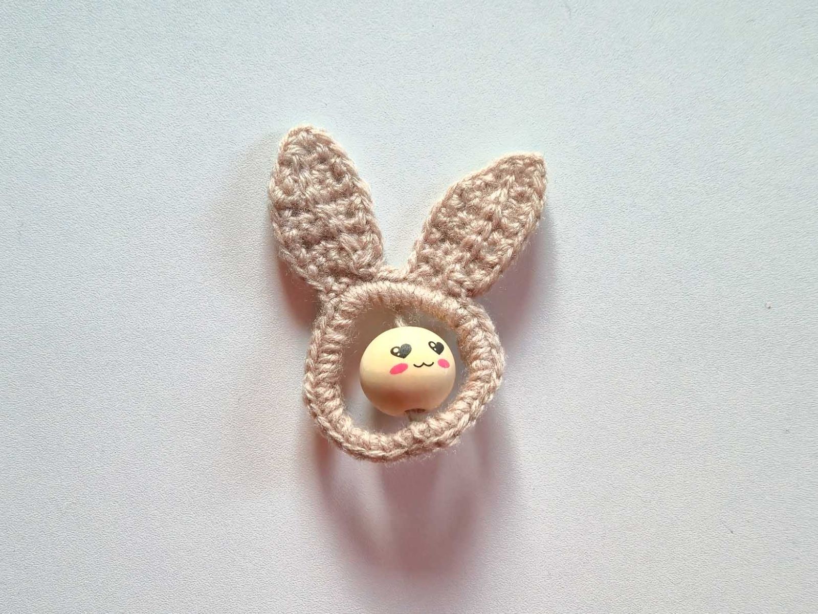 Das Bild zeigt den gehäkelten beigen Hasen Jumper mit einer Gesichtsperle dekoriert.