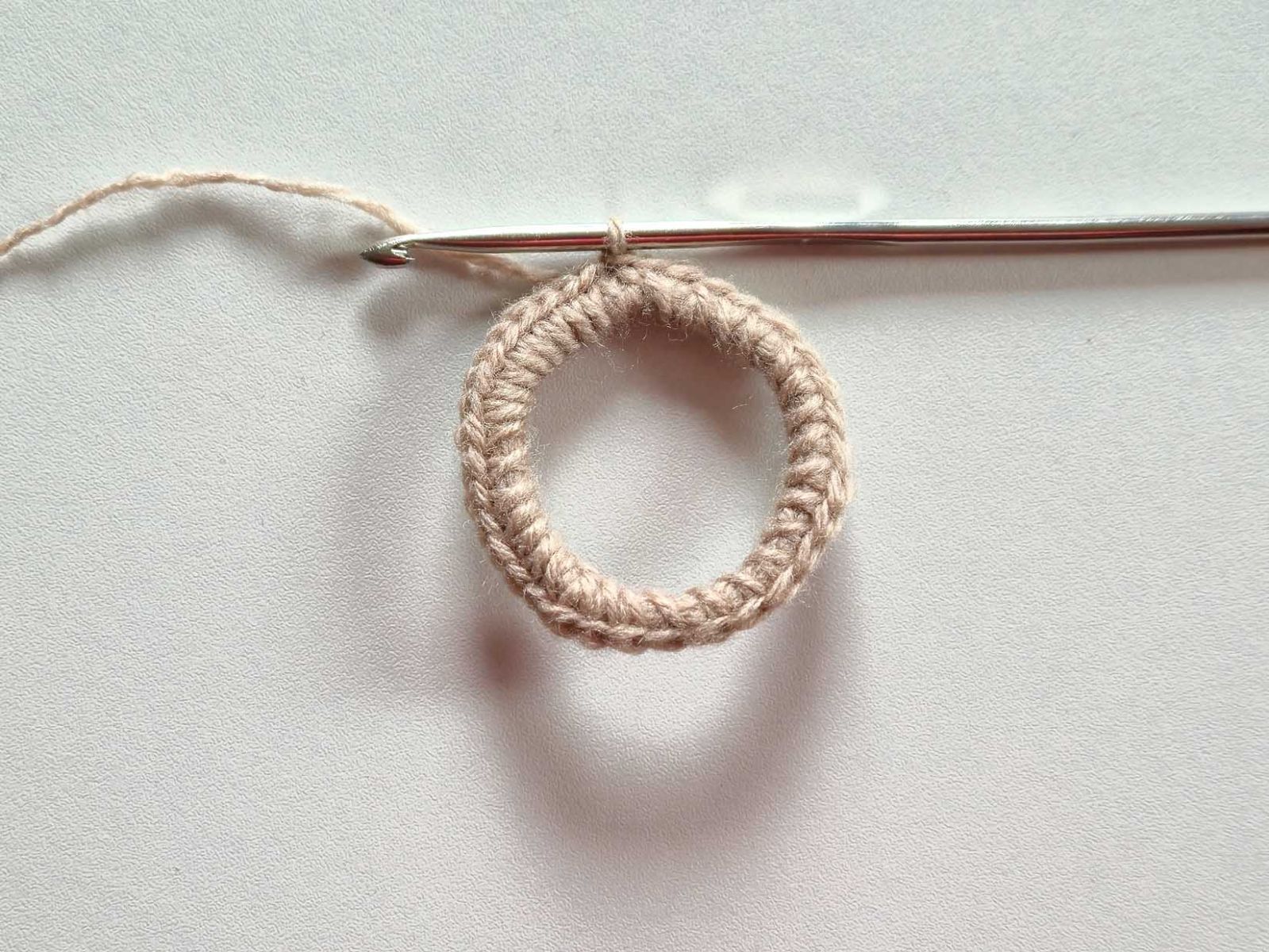 Ein Ring, gewickelt aus mehreren Runden beigem Garn wurde komplett mit festen Maschen umhäkelt und bildet nun einen stabilen Ring..