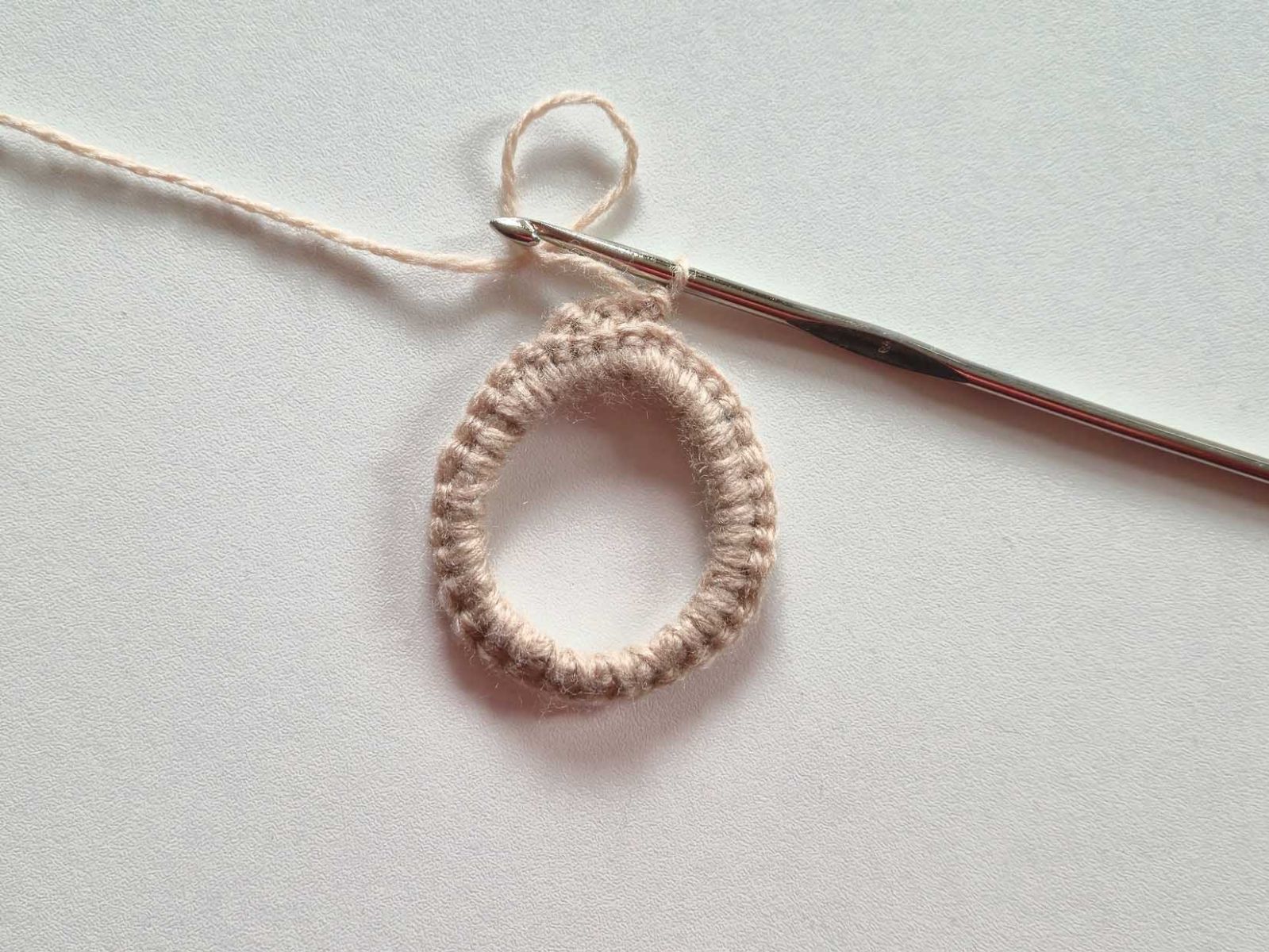 An dem beigen Ring wurde nun begonnen, das erste Ohr zu häkeln. Die Rückseite ist zu sehen.