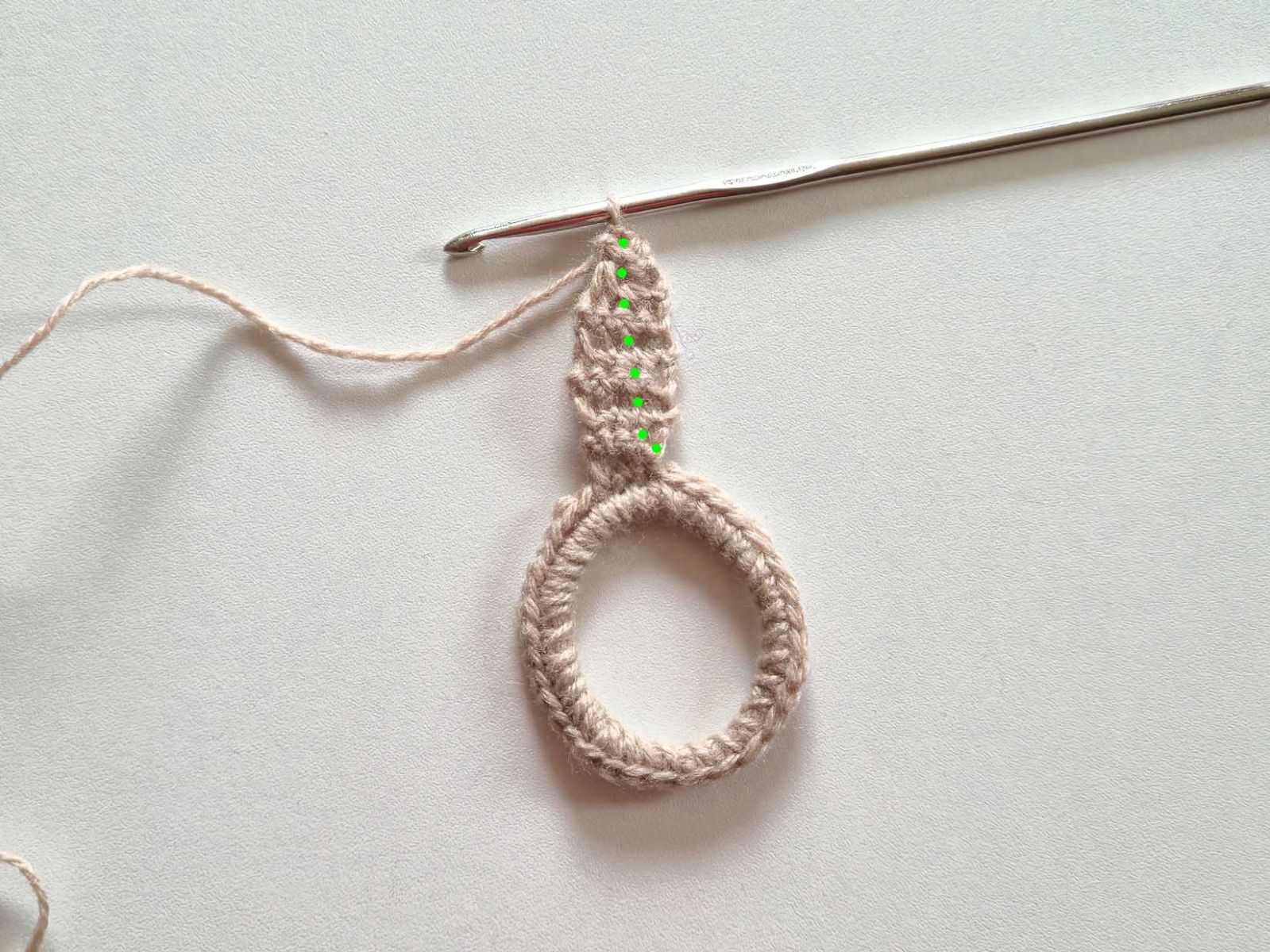 An dem beigen Ring wurde erste Ohr angehäkelt. Die Stellen zum Einstechen beim Weiterhäkeln wurden mit grünen Punkten markiert.