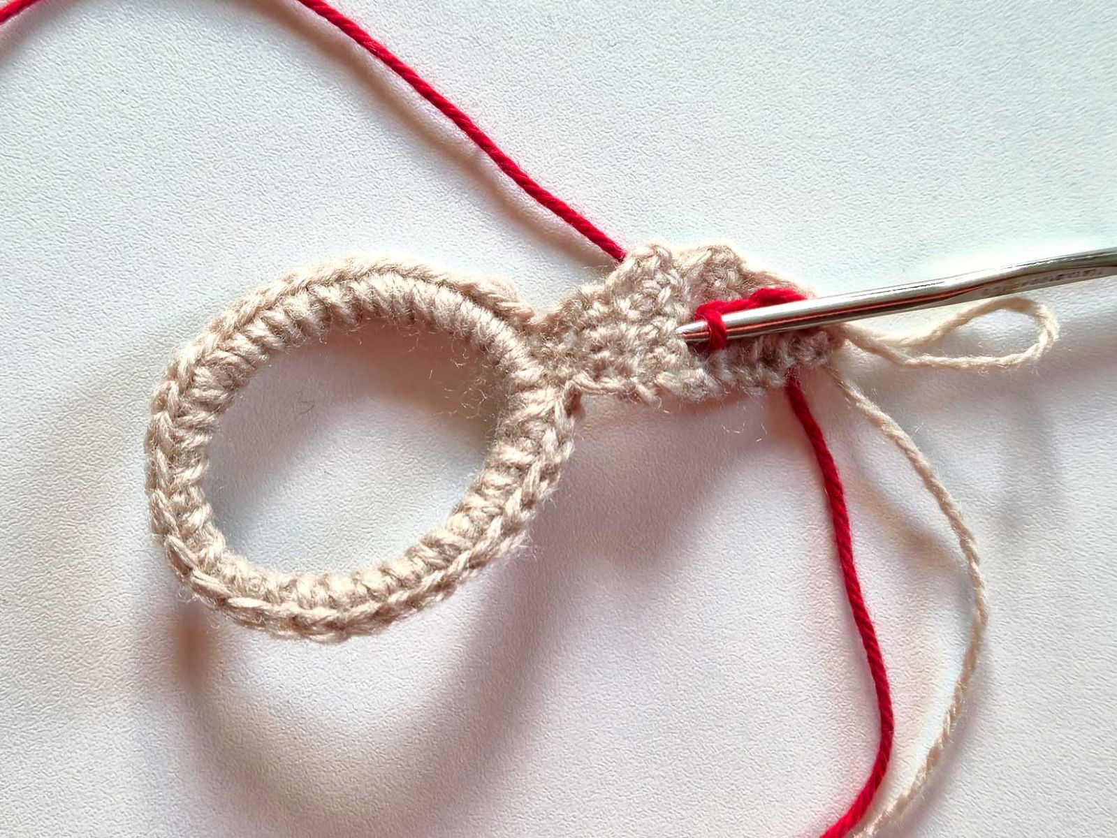 Das beige Ohr wurde zu Vorführzwecken mit rotem Garn weitergehäkelt. Das Bild zeigt das Einstechen der Nadel.