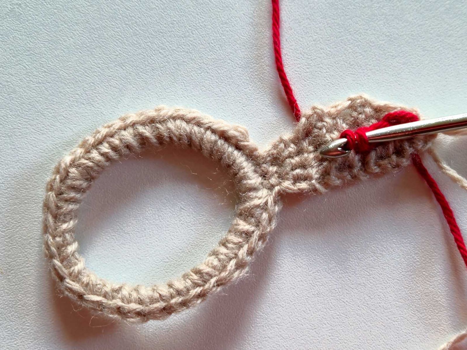 Das beige Ohr wurde zu Vorführzwecken mit rotem Garn weitergehäkelt. Das Bild zeigt das Durchziehen des Fadens durch das Ohr.