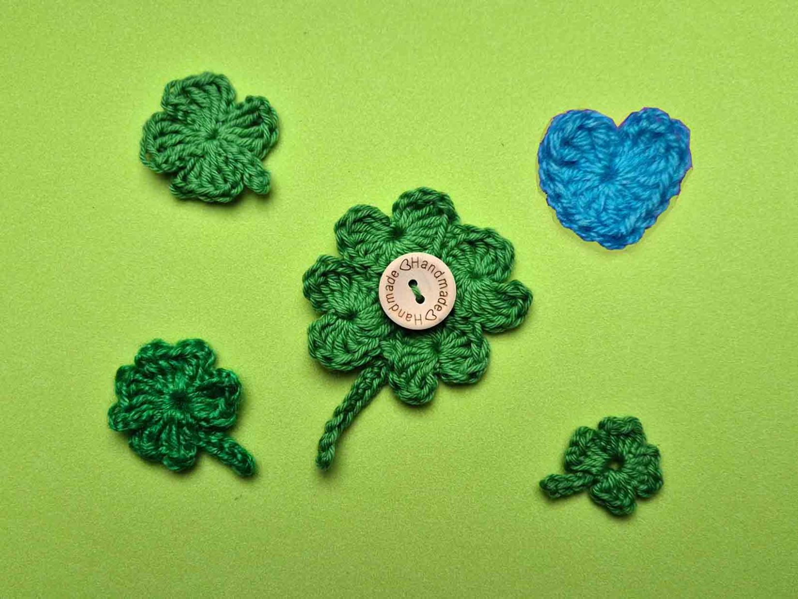 verschiedene Kleeblätter und ein blaues Herz liegen auf einem grünen Untergrund