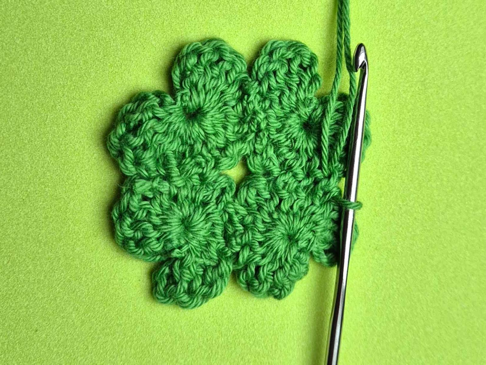 Der Faden wird neu angesetzt auf der Rückseite zwischen zwei Herzen. Damit wird der Stängel gehäkelt.