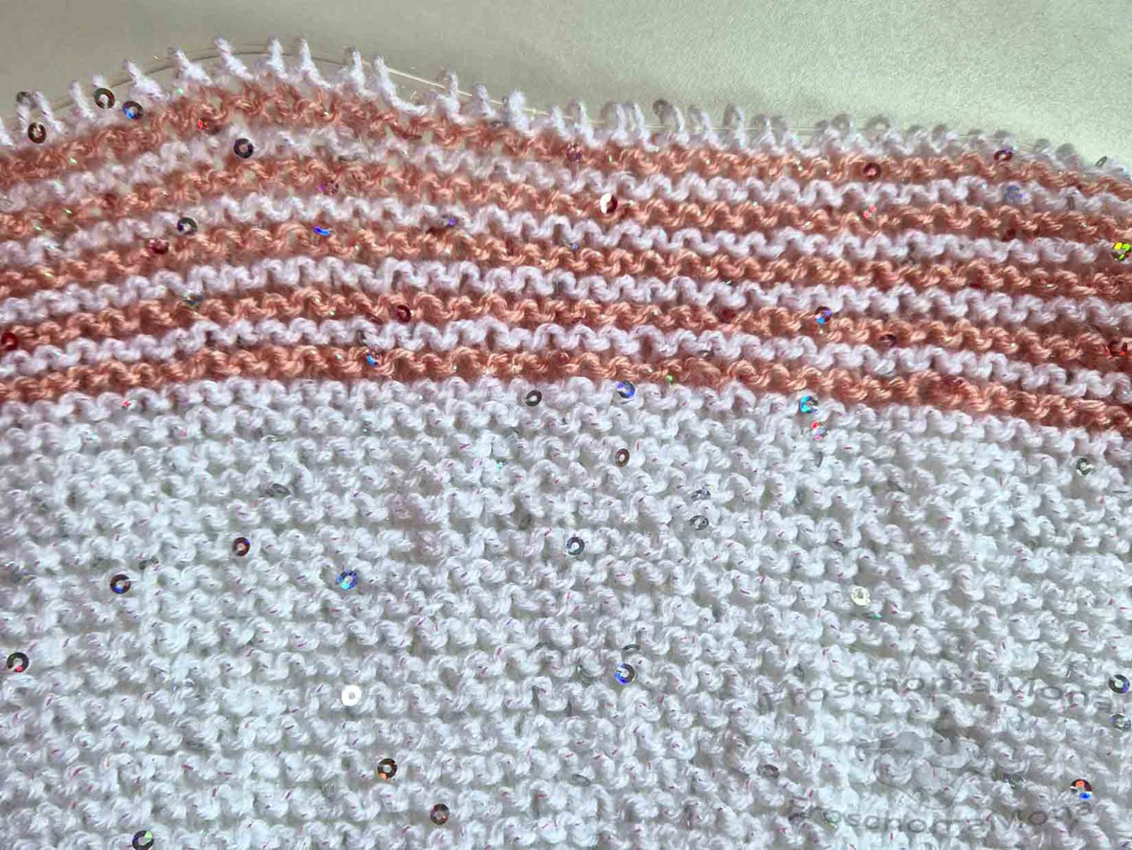 Ein kraus rechts gestricktes Schalstück in weiß einfarbig und weiß-rosa zweifarbig gestrickt, ist auf dem Bild zu sehen.