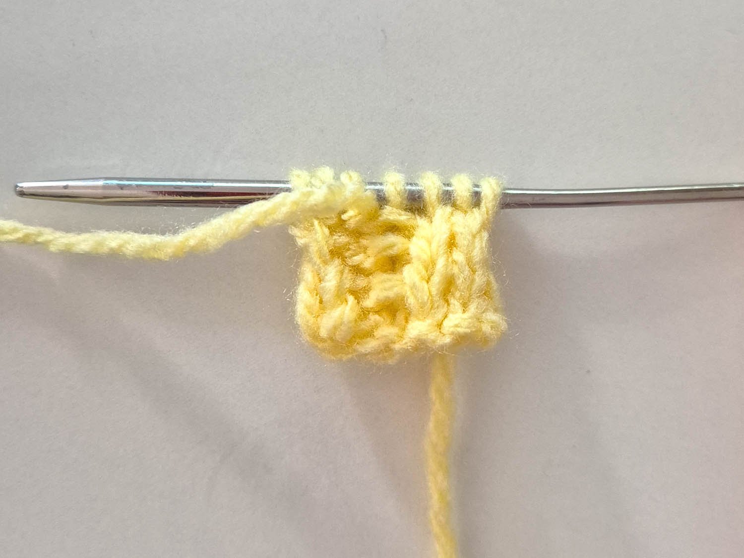 In gelber Wolle sind die gestrickten ersten Reihen zu sehen.