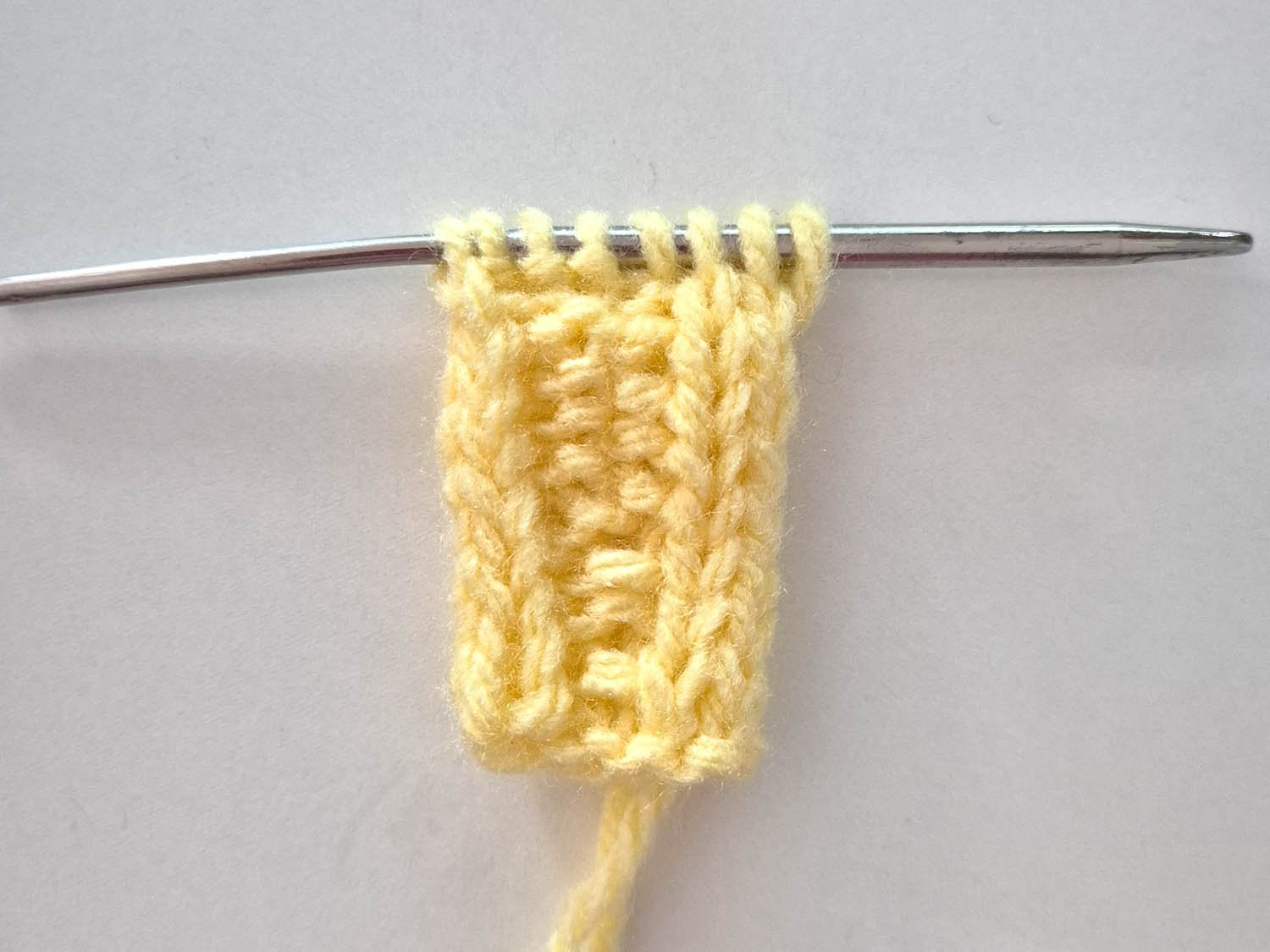 Der Anfang des Tuchs in gelber Wolle wird gezeigt. Der Anfangsfaden ist rechts unten.