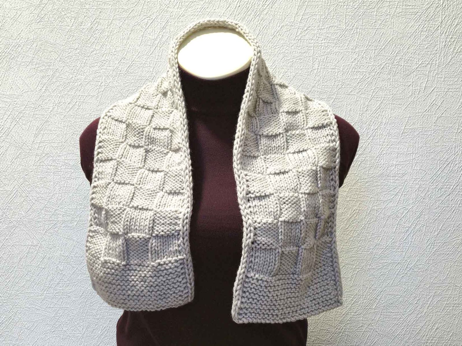 Ein hellgrauer Schal im Schachbrettmuster wurde einer Schaufensterpuppe ohne Kopf um den Hals gelegt.