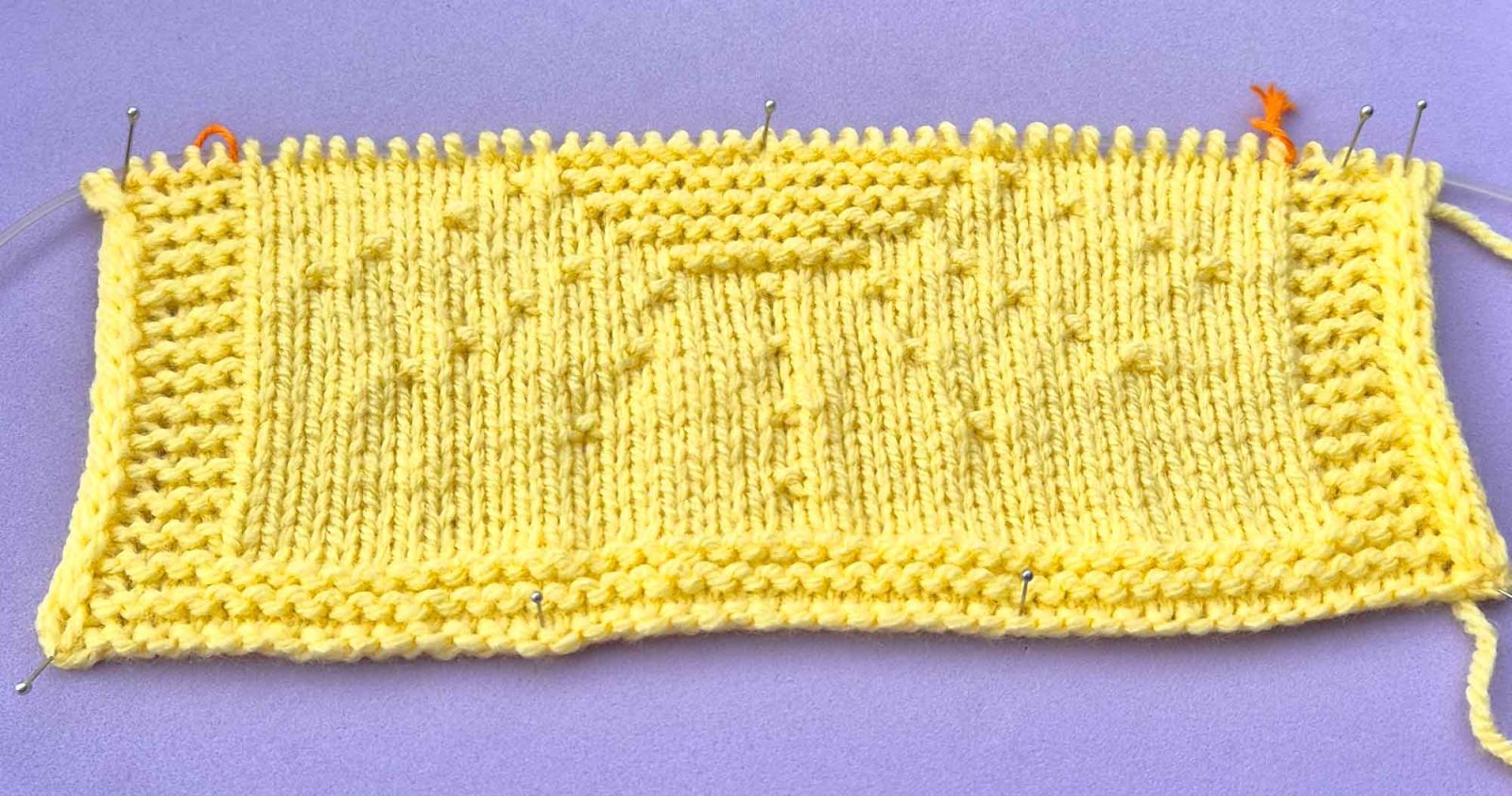 Das Strickbild der Sonne nach 30 gestrickten Reihen liegt auf einem fliederfarbigen Untergrund.