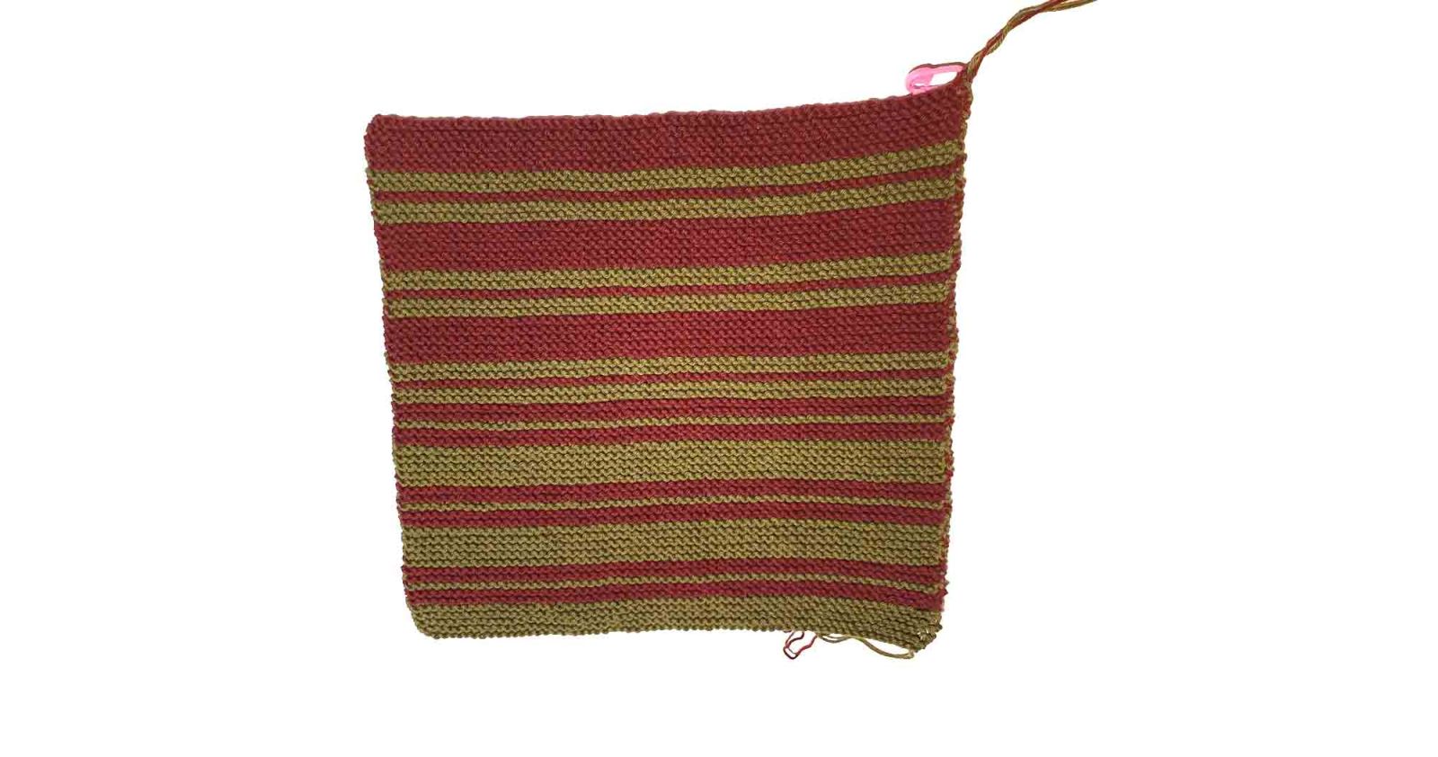 Der fertig gestrickte Topflappen ist zu sehen. Die Fäden sind noch nicht vernäht.