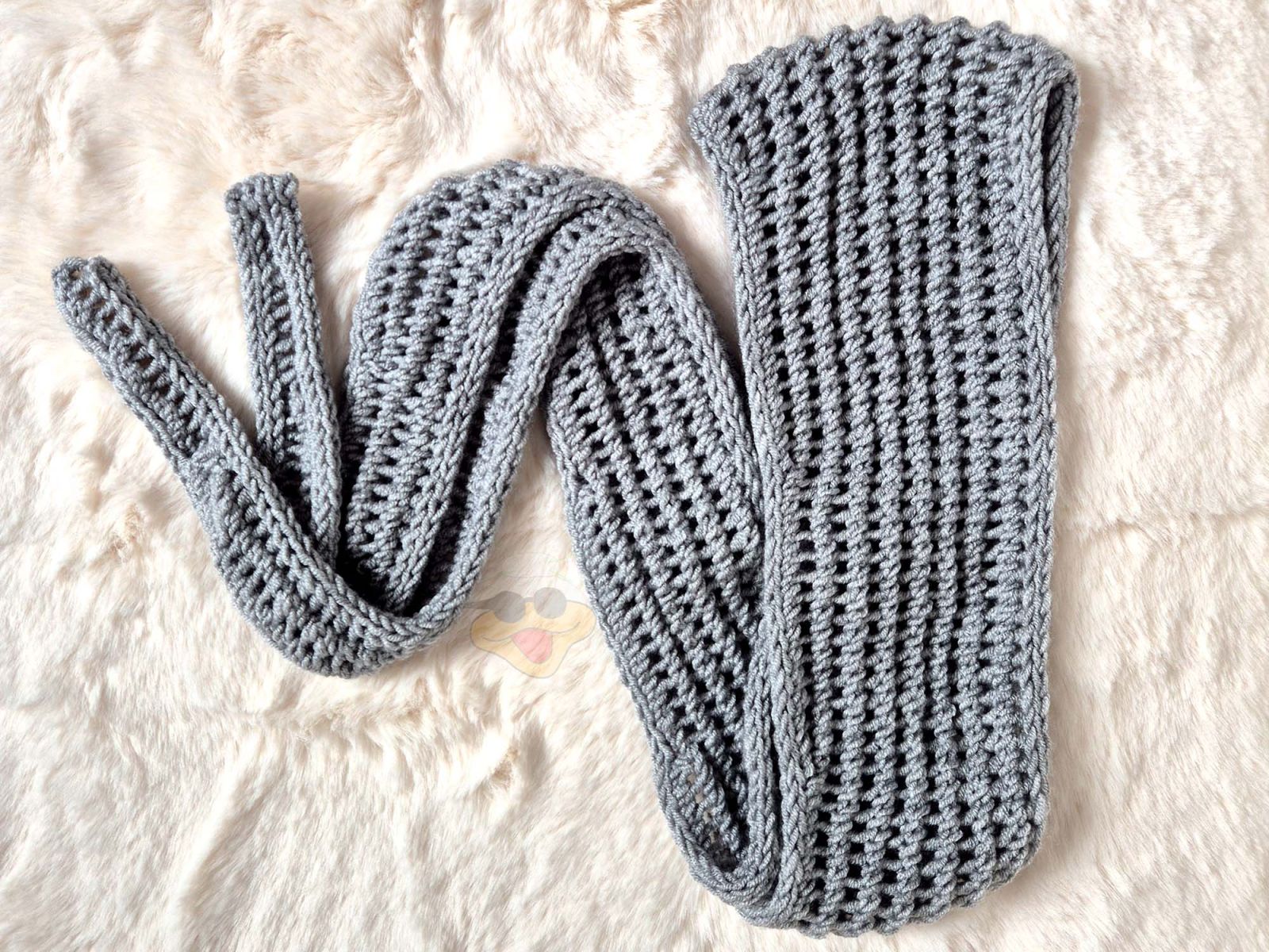 Ein graues gefaltetes Stricktuch liegt auf einem hellen Fell.