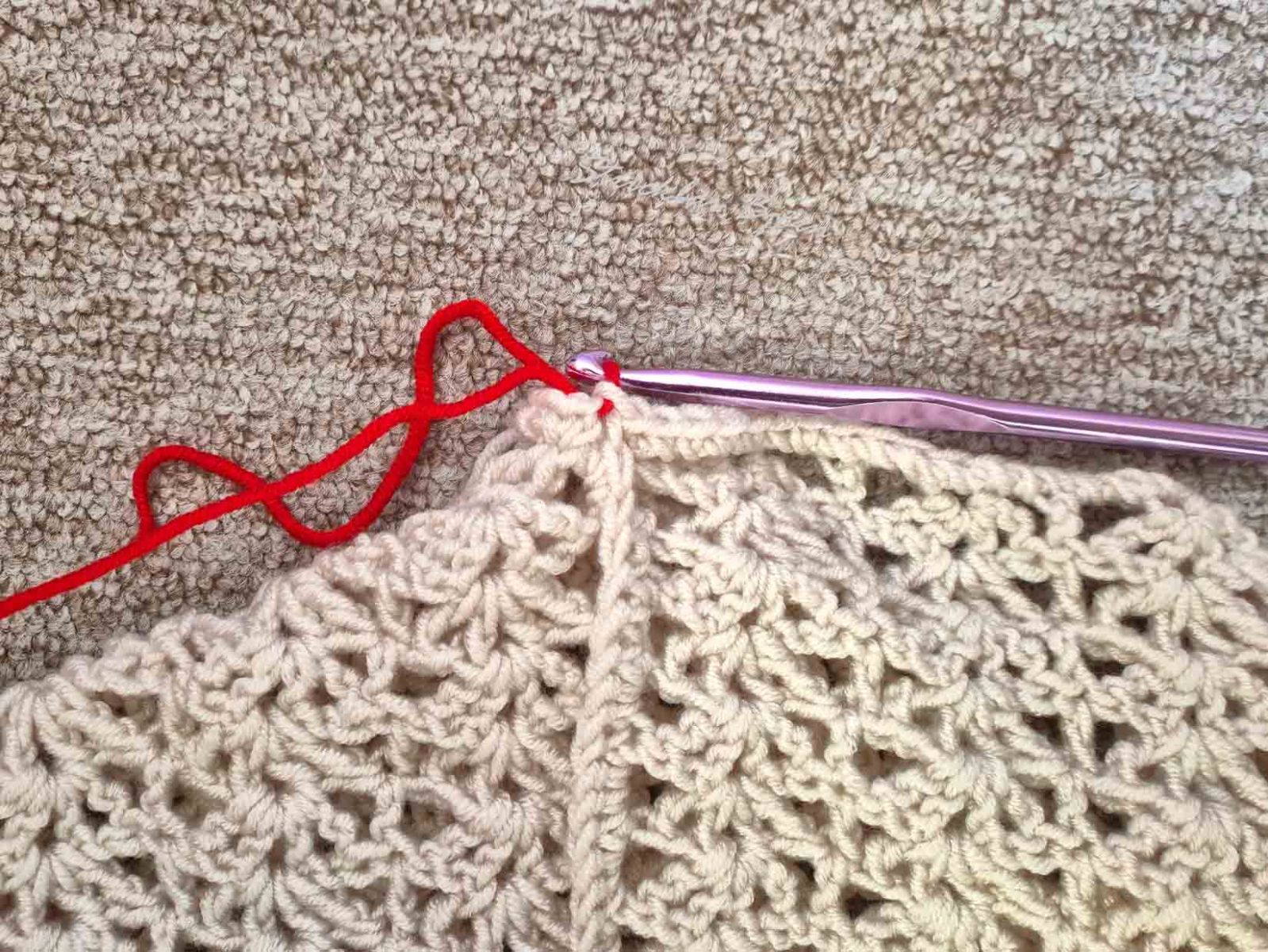 Das Bild zeigt das Durchziehen der Schlaufe bei der Kettmasche mit dem roten Garn.