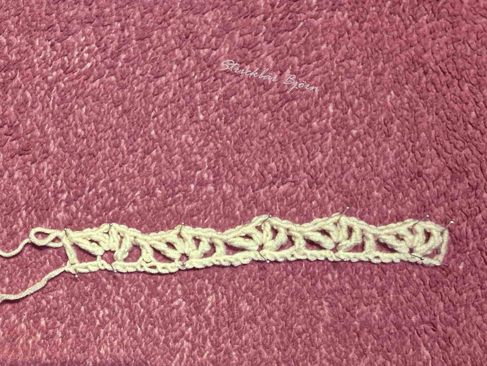 Das gehäkelte helle Wollteil liegt auf einem rosa Untergrund und zeigt, wie die erste Reihe gehäkelt aussieht.