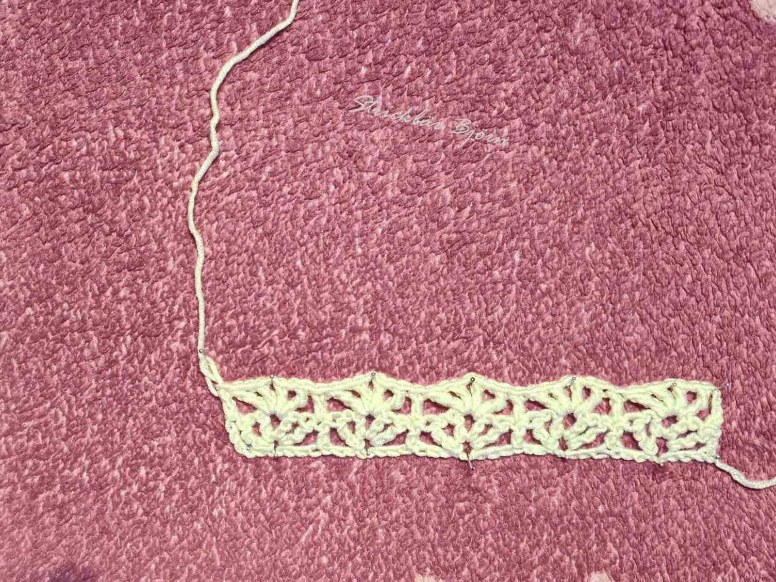 Das gehäkelte helle Wollteil liegt auf einem rosa Untergrund und zeigt, wie die ersten beiden Reihen gehäkelt aussieht.