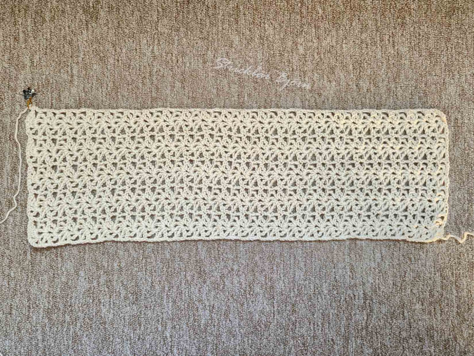 Ein gehäkeltes Rechteck liegt auf einem melierten Untergrund.