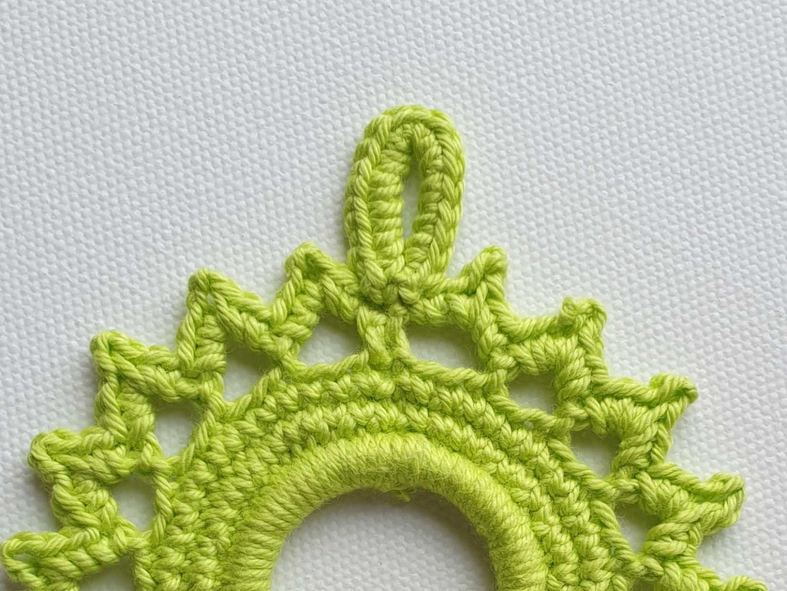 Es wird gezeigt, wie ein fertiger Aufhänger aus Luftmaschen und festen Maschen ausschaut.