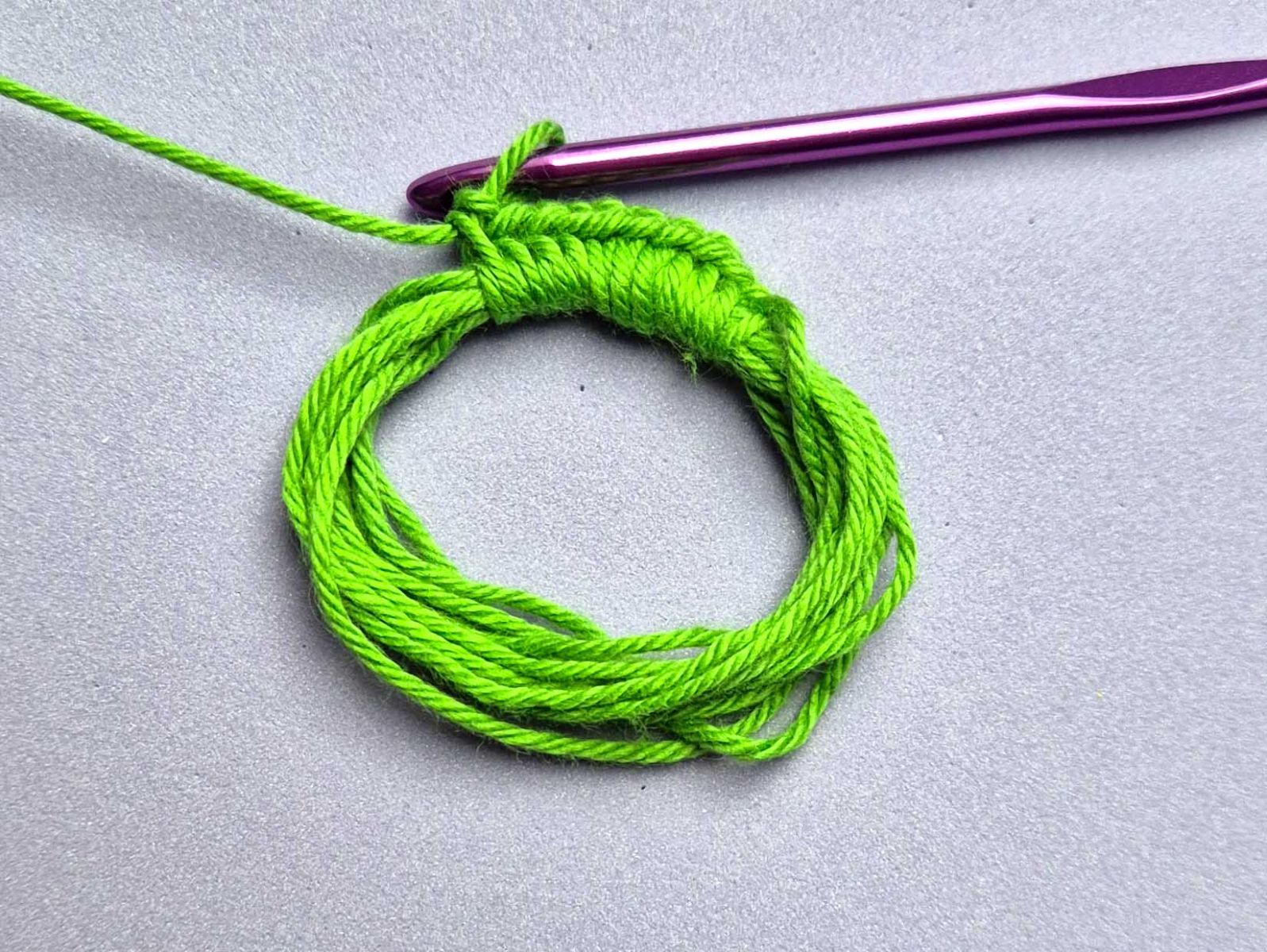 Ein Ring aus grünen Fäden wird mit festen Maschen umhäkelt.