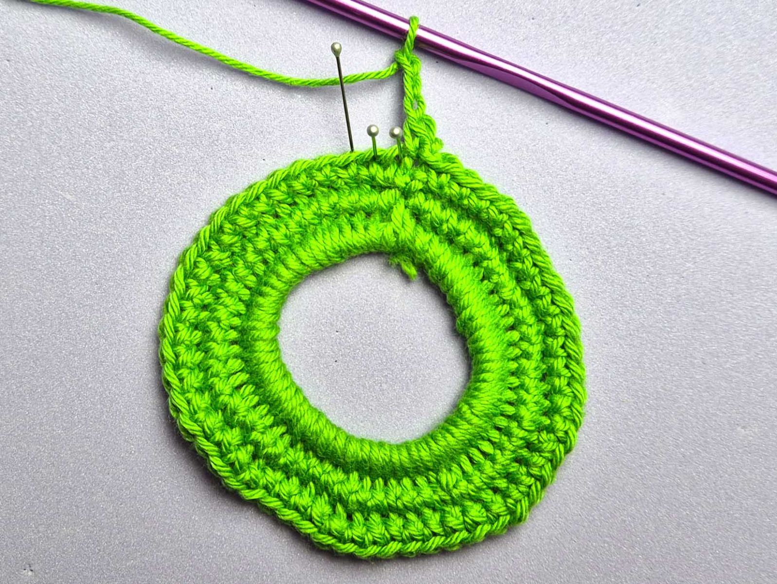 Der Beginn von Runde 4 wird gezeigt. Mit Stecknadeln wurden die Maschen gekennzeichnet, die übersprungen werden bzw. in die hinein gehäkelt wird.