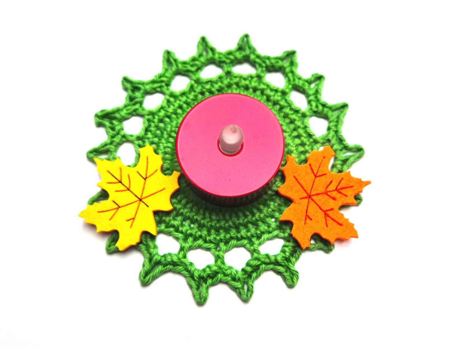 Ein grünes rundes Häkelstück mit vielen Zacken wurde mit einem Teelicht und zwei Ahornblättern dekoriert.