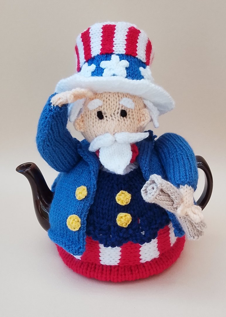 Hand‑knitted Uncle Sam tea cosy in patriotic outfit, saluting and holding the Declaration of Independence