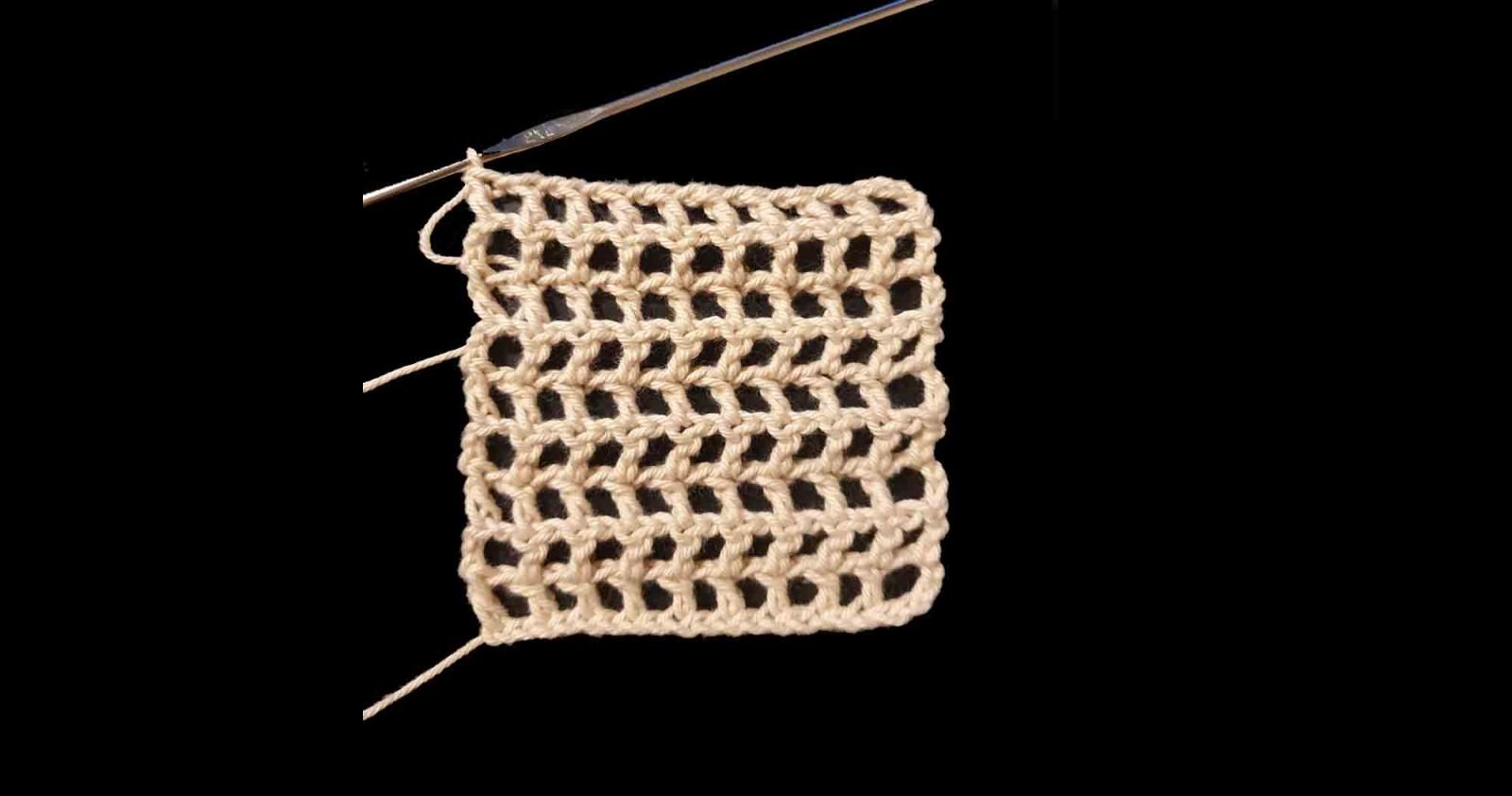 Das gehäkelte Gitter in hellem Garn liegt auf schwarzem Untergrund.