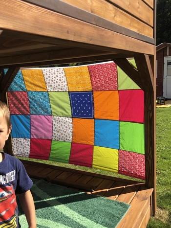 Ein Wind- und Sonnenschutz fürs Spielhaus. Dafür habe ich viele bunte gleichgroße Baumwollstoffteile (Reste, Tücher etc.) aneinandergenäht. Oben und unten habe ich noch ein stabiles Gummiband mit seitlichen Schlaufen angenäht.