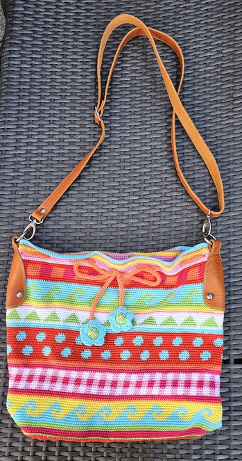 Ich habe mir vor etlichen Jahren schon die Anleitung zu dieser tollen Tasche gekauft, aber dann nie gehäkelt, weil ich andere Projekte hatte. Vor kurzem ploppte mir bei facebook in einer Vorschau auf einmal diese Tasche auf und ich verliebte mich erneut in sie🫶. Gerade als ich die Anleitung kaufen wollte, dachte ich, Mensch, da war doch was! Schnell flitzte ich in unser Büro und was soll ich sagen? Die Anleitung war fein säuberlich in einen meiner vielen Häkelordner abgeheftet! Also schnappte ich mir diese und wuselte in mein Schlafzimmer, in der ich kistenweise den Wollvorrat bunkere. Nun, ich verglich die Farben, einige hatte ich original gemäß Anleitung da, andere nicht. Diese ersetzte ich kurzerhand durch ähnliche Farben. Nach 6 Wochen häkeln, war die Tasche dann endlich fertig. Jedoch kam dann das Henkelproblem. Dem seinerzeit in der Anleitung aufgeführten online-Shop, wo die Henkel mal herstammten, gab es nicht nun nicht mehr, so dass ich auf die Suche ging. Ich wurde zwar fündig, ABER...so recht konnte ich mit den Henkeln nicht anfreunden. Warum nicht? Sie sind zwar wunderschön und ich mag das rot mit den weißen Punkten sehr, aber letztendlich stellte ich mir die Frage: Wie willst du die Tasche benutzen? Nun da fiel mir ein anderes Häkelprojekt ein und an dieser Tasche hatte ich in einem hiesigen Lederwaren-Fachgeschäft mir auf meine Bedürfnisse abgestimmt, Henkel anfertigen und anbringen lassen. So habe ich die Tasche dort hingebracht und nach 2 Wochen konnte ich sie wieder abholen.  Jetzt ist die Tasche für mich perfekt, die Henkel sind komplett abnehmbar und ich kann die Tasche, falls sie mal schmutzig werden sollte, auch waschen. Ihr seht mich also total happy😁.
Die Anleitung war gut geschrieben bzw. beschrieben, so dass mir das häkeln danach leicht gefallen ist und zumal ich ja auch ein großer Fan von Häkelschriften bin.
Ich trage heute, am 4.3.2026, das erste Mal die Tasche spazieren und freue mich schon auf die Kommentare dazu.
Danke an dieser Stelle noch einmal für diese tolle Tasche und die Farbinspiration🫶...und insbesondere noch einmal für die tolle Anleitung❤️