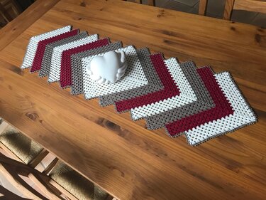 Crocheted zigzag table runner of red, white, and brown granny squares on a wooden table with a small white ornament