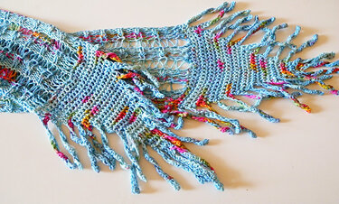 Nahaufnahme eines hellblauen gestrickten Schals mit offenem Muster und gedrehten bunten Fransen