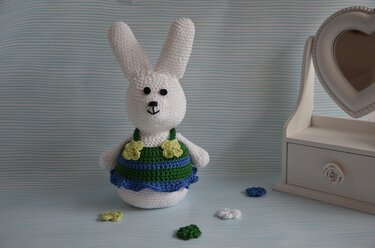 Weißer gehäkelter Amigurumi-Hase mit blau-grünem Kleid und hellgrünen Blüten