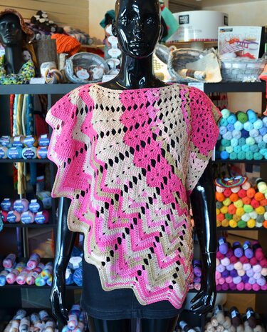 Gehäkelter Damen-Poncho mit Zickzack-Lochmuster und welligem Saum in Pink und Beige an einer Schaufensterpuppe