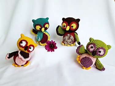 Four colorful crocheted amigurumi owls with a purple flower on a white background.