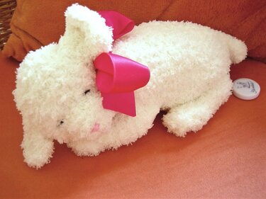 Weißes flauschiges gehäkeltes Lamm mit pinker Schleife auf orangefarbener Fläche.