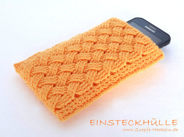 Orangefarbene gehäkelte Einsteckhülle mit Zopfmuster und teils sichtbarem schwarzen Smartphone