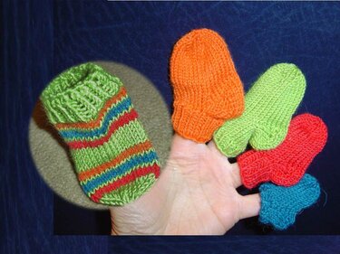 Hand mit gestrickter, grün gestreifter Babysocke und vier bunten Fingerlingen