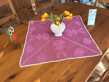 Quadratisches rosa gehäkeltes Deckchen mit weißer Muschelkante und Tulpenvase