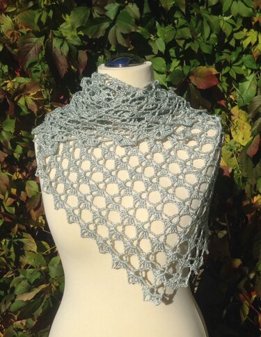 Light grey crocheted lace shawl draped on a mannequin with leafy background.