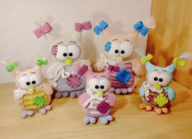Fünf gehäkelte Amigurumi‑Eulen in verschiedenen Größen mit Schleifen und aufgestickten Flicken am Bauch.