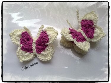 Zwei gehäkelte Schmetterlinge in Creme und Magenta auf heller Fläche