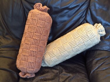Zwei gehäkelte Nackenrollen in Braun und Beige mit Korbmuster auf einem Ledersofa