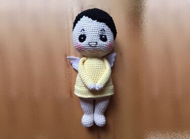 Gehäkelte Amigurumi-Engelpuppe in gelbem Kleid mit schwarzen Haaren und weißen Flügeln