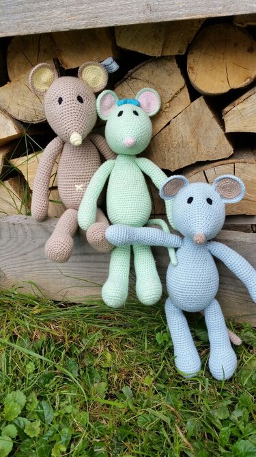 Nahaufnahme dreier Amigurumi-Mäuse in Pastell mit betonten Ohren und Gliedmaßen vor Holzstapel